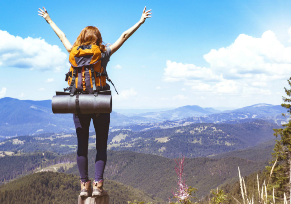 Hiker celebrating freedom to travel atop a mountain with expansive views, embodying the spirit of adventure and comprehensive travel insurance coverage.
